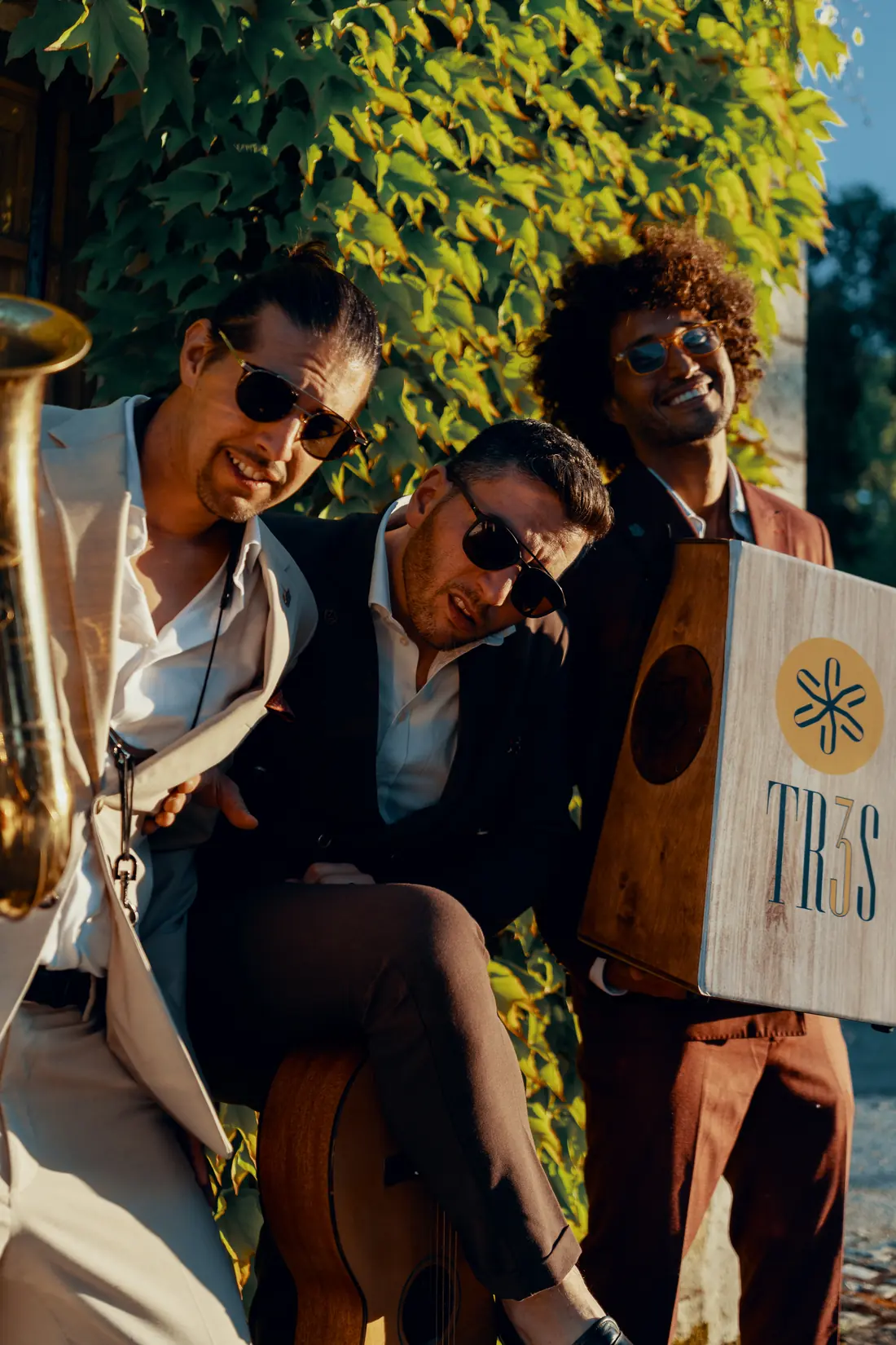 The trio close to the camera among green ivy, the saxophone in the foreground and the TR3S cajon on the right