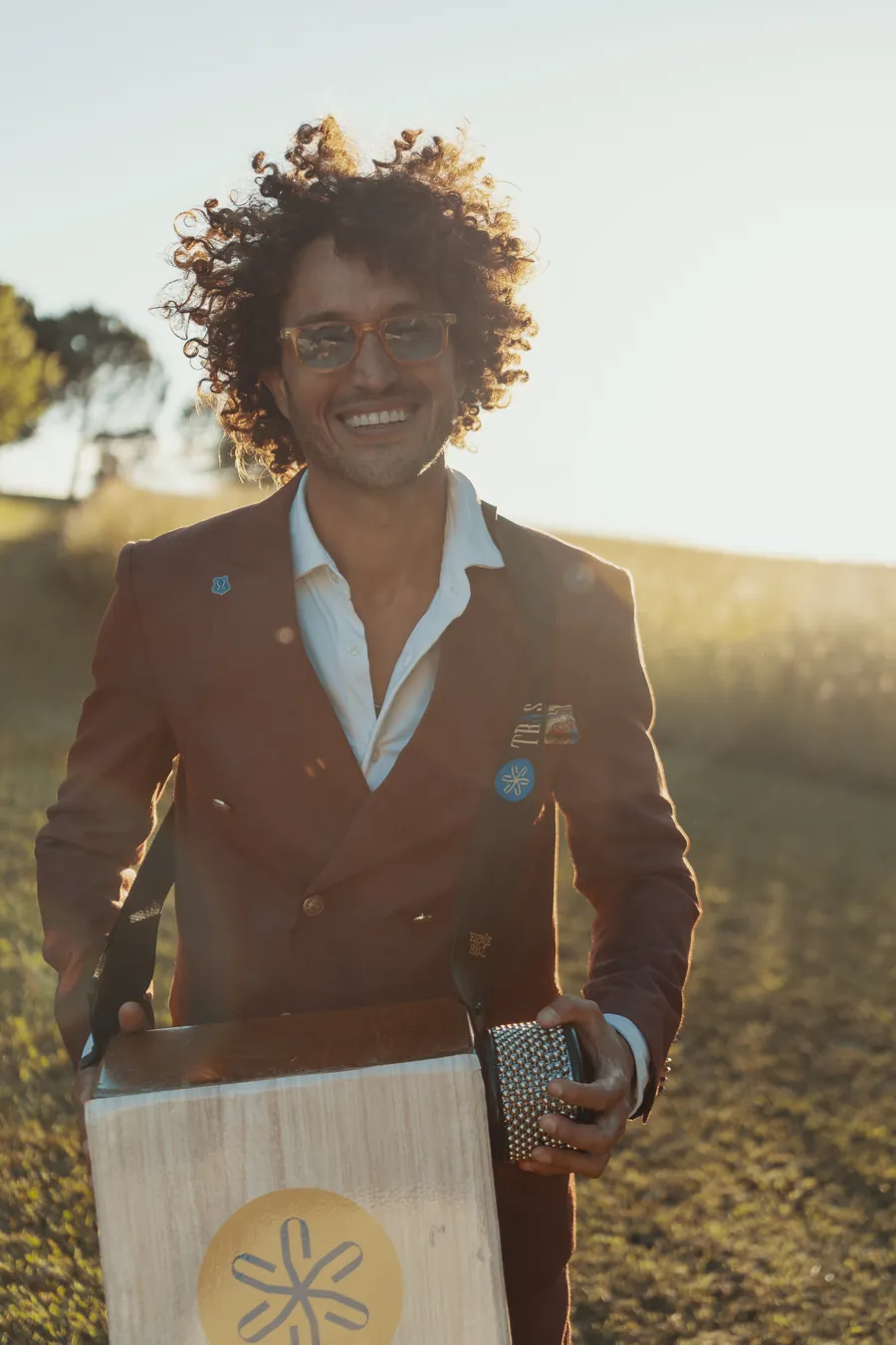Andres, the TR3S percussionist, with curly hair and a terracotta jacket smiling behind his TR3S cajon