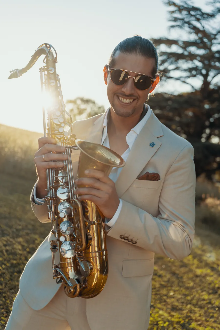 Manu, the TR3S saxophonist, in a cream suit smiling at the camera in golden evening light